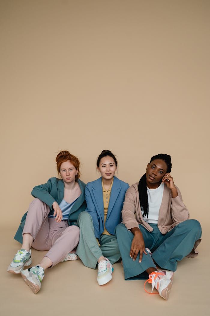 Three diverse women in pastel outfits sitting against a beige background, exuding elegance and style.